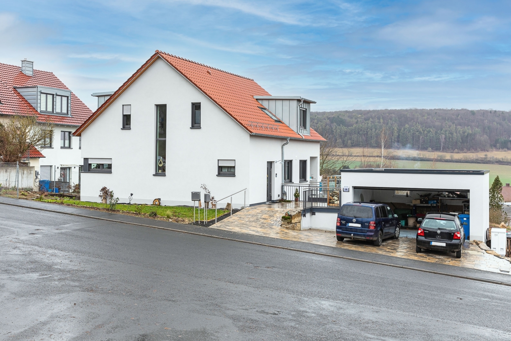 großes weißes Wohnhaus mit Garage; im Hintergrund Wald und Felder